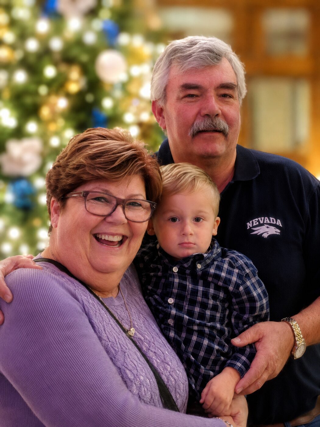 Andrea and Dan with a grandchild in front of a Christmas tree