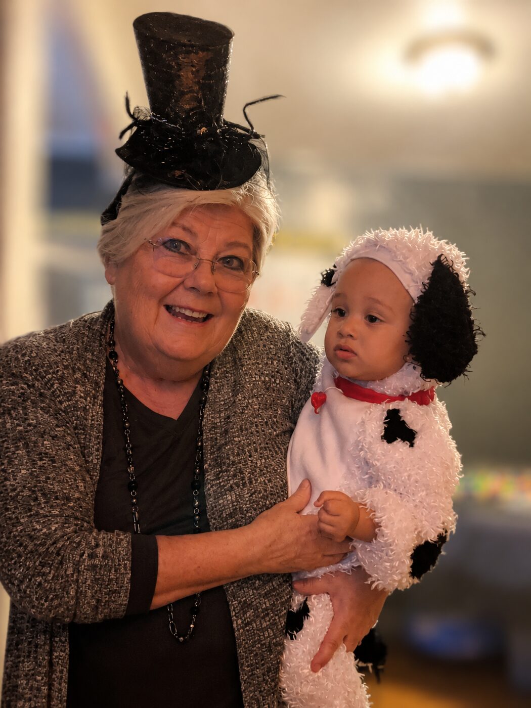 Andrea in a top hat holding a grandchild in a puppy costume at Halloween
